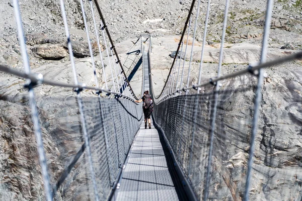Female hiker walking on the hanging bridge over the Glacier de Corbassiere on a mountain trail around Valais Swiss Alps.