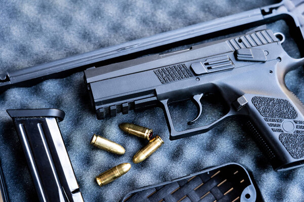 Close up view of bullets and handgun. Small black pistol next to a 9 mm bullets and a magazine. Shallow depth of field.