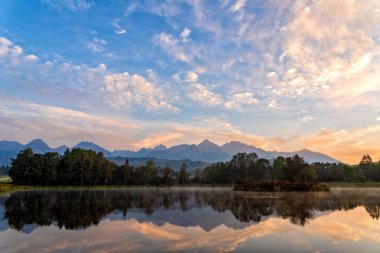 Güzel sonbahar dağ manzarası göl, renkli ağaçlar ve yüksek tepeler ve altın gökte Yüksek Tatras, Slovakya ile huzurlu sahnenin gündoğumu atış.