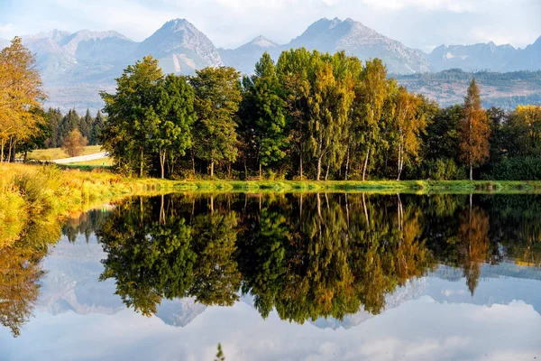 Peaceful scene of beautiful autumn mountain landscape with lake, colorful trees and high peaks in High Tatras, Slovakia.