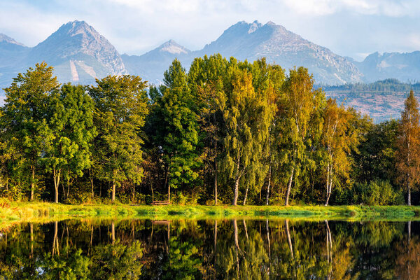 Peaceful scene of beautiful autumn mountain landscape with lake, colorful trees and high peaks in High Tatras, Slovakia.