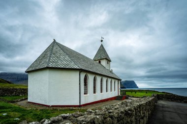 Faroe Adaları 'ndaki tipik beyaz köy kilisesi dramatik manzarayla çevrilidir..