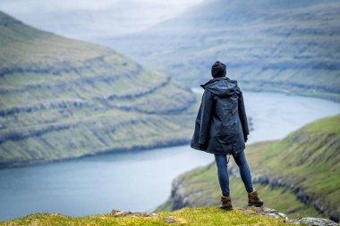 Dağın tepesinde duran kadın gezgin Faroe Adaları fiyortlarının muhteşem manzarasının tadını çıkarıyor..
