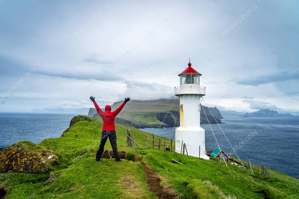Young female hiker enjoying a spectacular view of lighthouse on Mykines island in Faroe Islands.