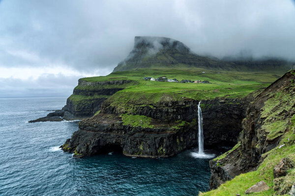 Scenic view of popular Mulafossur Waterfall with the village Gasadalur in background, Faroe Islands.