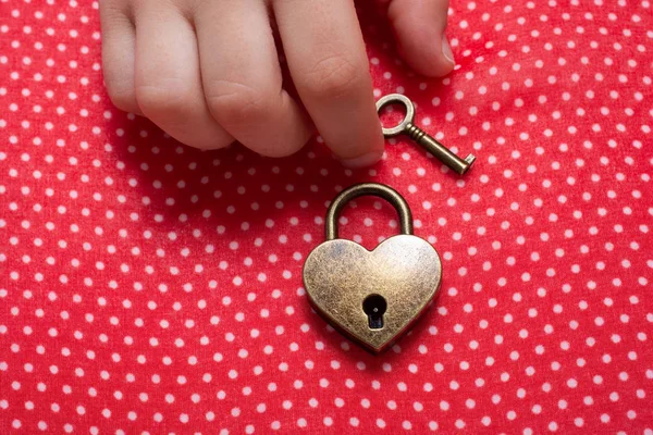 Hand holding a heart shaped lock and key on red background