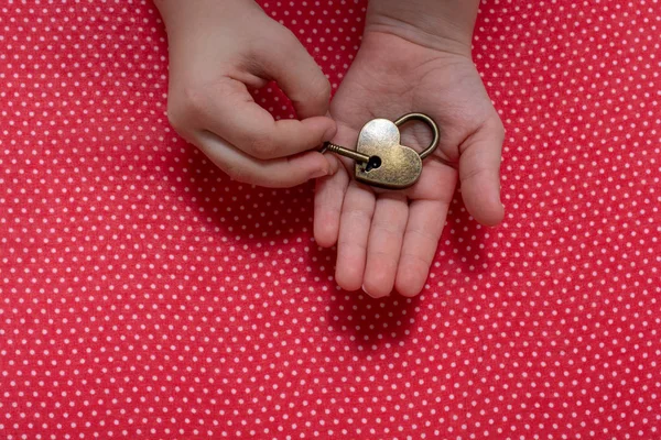 Hand holding a heart shaped lock and key on red background