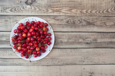 Sarı-kırmızı ve turuncu kiraz berry dokular bir hasır sepet içinde hafif bir ahşap zemin üzerine yeşil yaprakları ile.