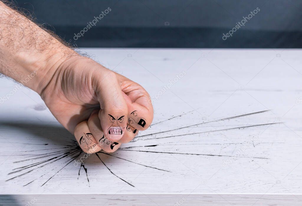 Fist hitting table with violence, with cartoons on the fingers simulating bullying, male violence, gender violence and domination