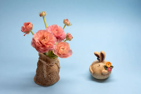 Cute bouquet of delicate pink buttercups and hare figurines on a blue background — Stock Photo, Image