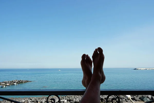 Deniz manzaralı otel balkonunda erkek bacakları — Stok fotoğraf