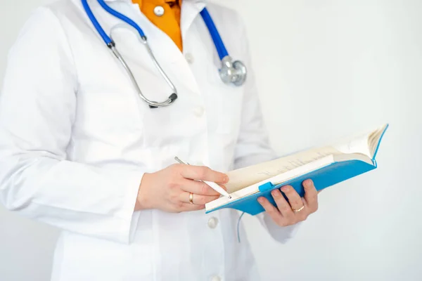Kadın doktor hastanedeki panoya notlar yazıyor. Stetoskop ve not defteri olan beyaz önlüklü bir doktor..