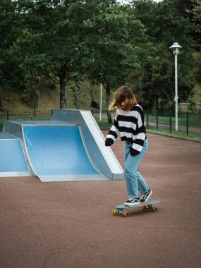 Genç bir kadın kaykay parkında paten kayıyor.