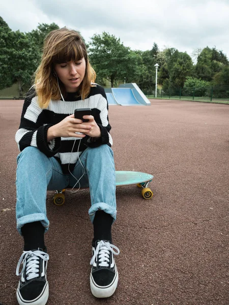 Mujer joven revisando su teléfono inteligente y escuchando música —  Fotos de Stock