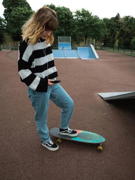 Genç bir kadın akıllı telefonunu kontrol ediyor ve müzik dinliyor.