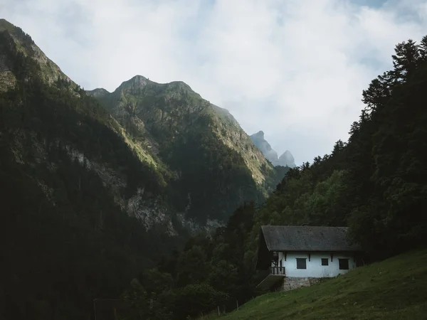 Pequeña casa blanca en una colina verde con grandes montañas en el fondo — Foto de Stock