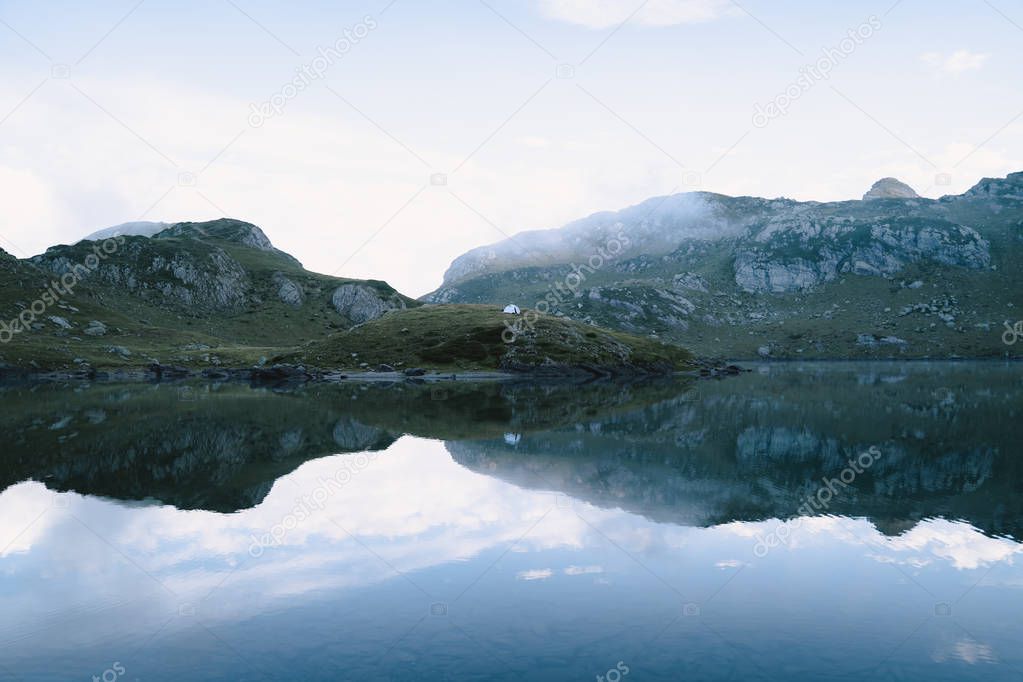 Calm water lake mirror reflection of the mountains on a foggy day