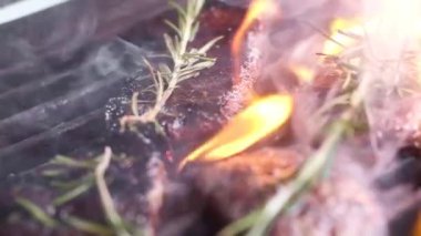 mermer biftek. Yüksek ateşte kızartılır. Çerçevede alevler ve duman var. Hafta sonu barbekü. Et kokulu kekik. Kamera hareket eder, odağı değiştirir. yakın çekim, yavaş çekim