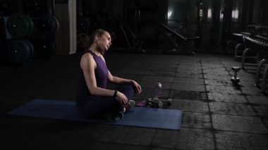 Genç ve güzel bir kız spor salonunda egzersiz yapmadan önce başını ve boynunu yoğurur. Yerde oturuyor ve aktif olarak kafanın dairesel hareketlerini yapıyor..