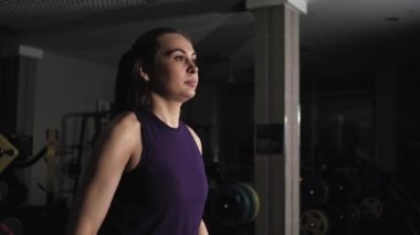 Spor salonunda egzersiz yapan genç ve güzel bir kız. Metal dambıllarla el kaldırın. Kollarını yana açıyor..