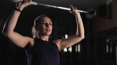 ince genç kız bir halter ile egzersiz yapıyor. Ağırlık iniş ve iner. Spor salonunda akşam antrenmanı.
