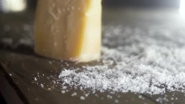 Parmesan peyniri parçası ahşap bir masa üzerindedir. Etrafta bir sürü rendelenmiş peynir var. Odak hareket ediyor. yakın çekim.