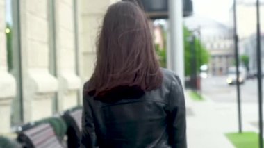 gri eşarp, siyah deri ceket ve kot sokakta yürürken güzel neşeli genç kadın. Arkasını döner ve kameraya kışkırtıcı bir şekilde güler. Rüzgarda çırpınan uzun saçlar