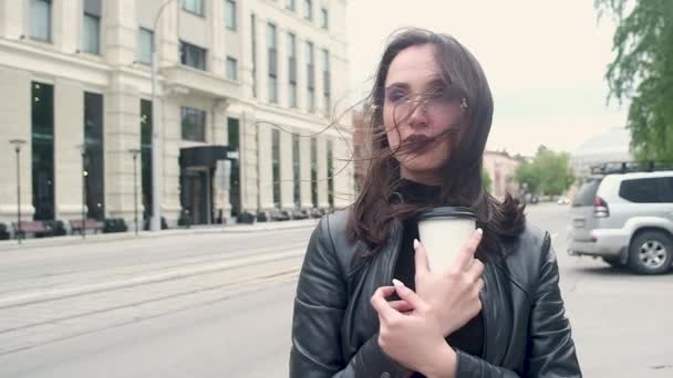 재킷과 안경을 소녀는 차가운 바람에 커피를 있습니다 머리를 합니다 배경에 — 비디오