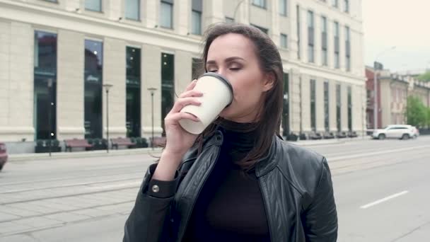 재킷에 매력적인 소녀의 초상화 차가운 바람에 컵에서 커피를 마시고 있습니다 — 비디오