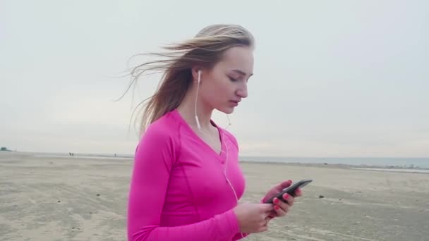 Menina Praia Uma Camisa Esportes Ouvindo Música Telefone Através Fones — Vídeo de Stock