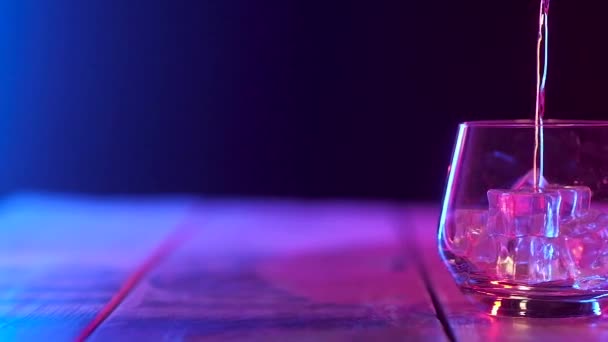 在玻璃透明滚筒与冷冰块 站在木桌上 倒旧浓郁的威士忌 摄像机从左到右平稳移动 带多色照明的全景拍摄 — 图库视频影像