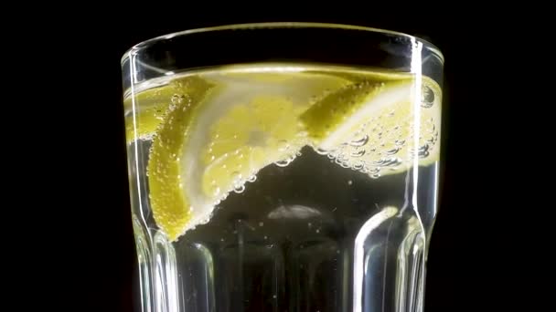 Einem Transparenten Glas Mit Kohlensäurehaltigem Wasser Schwimmenden Scheiben Gelber Zitrone — Stockvideo