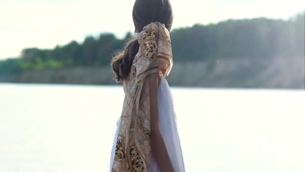 해안의 배경에 그녀의 머리에 드레스와 스카프에 머리와 날씬한 아름다운 소녀의 — 비디오