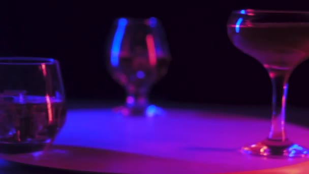 圆形木制旋转支架开始旋转 有好酒杯白兰地 威士忌 马提尼 在玻璃熔化的玻璃杯中清除冷冰 黑色背景上的条形照明 — 图库视频影像