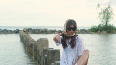 beyaz bir elbise genç güzel kadın, kafasına renkli bir mendil, bir sandalet ve büyük siyah güneş gözlüğü suda duran dikdörtgen taşlar üzerinde sıkışmış bacağı ile oturur. Sıcak yaz akşamı