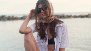 beyaz düğmesiz elbise ve siyah bir mayo genç güzel seksi kız, kafasına bir mendil ile, kamera için poz büyük siyah güneş gözlüğü, onu siyah saç ayarlama. Yakın çekim.