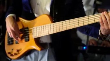 Mavi takım elbiseli Genç adam, beyaz gömlek ve gri pantolon bir konserde sahnede sarı bir elektrik bas gitar oynar. Vücut taşır ve müziğin yendi kalın dizeleri parmak