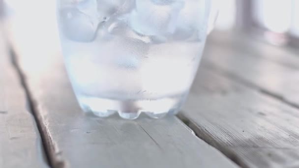 un grand pichet en verre transparent et embrumé avec glaçons froids se dresse sur une table en bois gris. lumière naturelle du jour. La caméra monte. .