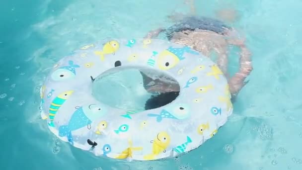 少年は水の下で泳ぎ 浮き上がれ 正確に膨張可能な円で頭を打つ 彼はカメラを見て 笑顔と貪欲に空気を吸い込みます 暑い夏の日にホームフレームプールで泳ぐ スローモーション — ストック動画
