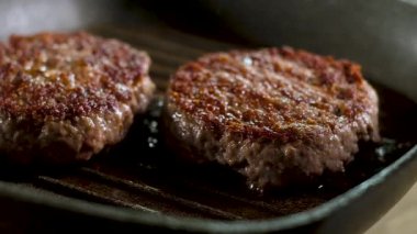 gevrek kahverengi kabuk ile iki et yağ sulu burger sıcak bir ızgara tavada kızartılır. Isıtmalı Kaynar sıcak tereyağı sıçrar. Mutfakta Pişirme sürecinin panoramik yavaş çekim resmi.