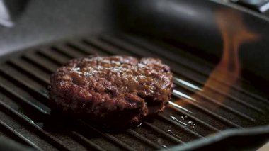 çıtır kahverengi kabuk ile sıcak lezzetli sulu kızarmış et Burger Patty, parlak bir alev ızgara tavada yatıyor. Mutfakta flamb et pişirme yavaş hareket. kamera geri hareket
