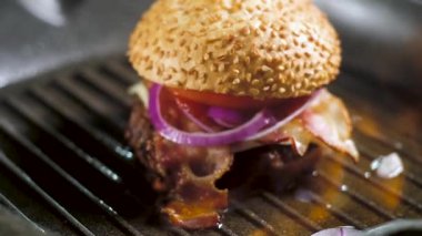 büyük metal tava ızgara yanan alev üzerinde. Susam ile ateş Burger, kabuk, pembe soğan halkaları, işlenmiş peynir, kırmızı domates ve gevrek pastırma ile kızarmış Patty. Mutfakta flamb süreci.