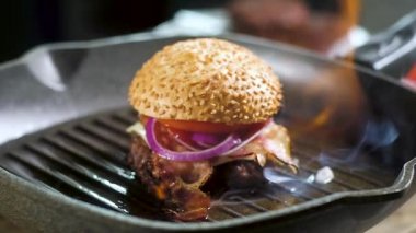 Taze pişmiş burger bir ateşin ateşinde bir tavada yanar. Susamlı yanmış çörek. mutfakta flamb