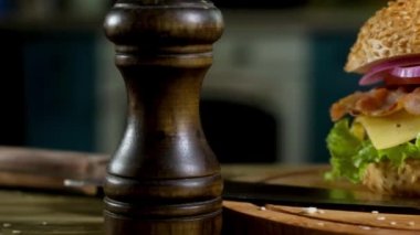 mutfakta, masada karabiber shaker, keskin bıçak ve olgun domates, susam, salata, kızarmış pirtikola, peynir dilim, ahşap standı nda sos pastırma ile topuz hamburger. Panorama çekimi