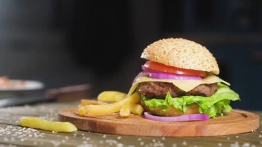 Sulu kızarmış pirtivar, peynir ve pembe soğan halkaları bir dilim ile Burger mutfak arka planda ahşap bir tepsi üzerinde yatıyor. patates kızartması ile yakın