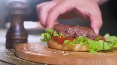 şef yeşil taze marul yaprağı ve domates sosu ile topuz üzerinde kahverengi gevrek kabuk ile iyi kızarmış Burger koyar. Yukarıdan peynir ince dilim terk etmektir. yakındaki bir siyah retro biber shaker duruyor.