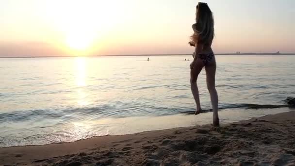 色の水着で細い美しい女の子と長い髪で暖かい水に実行され 夕日に対して海で泳ぐ 夕方の光のスローモーション — ストック動画