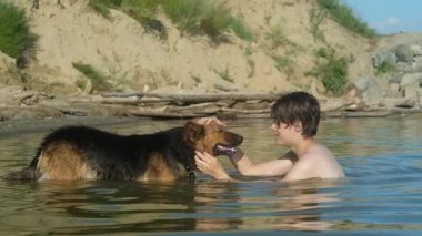 Denizde bir köpekle banyo yapan bir adam. Boynunda tasma olan Alman çoban köpeği suyun içinde. Adam onu okşuyor ve kulağını tırmalıyor. Arkadaşlık ve hayvanlarla ilgilenme kavramı..