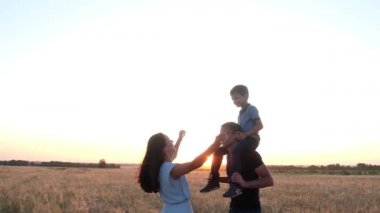 oğulları yla birlikte bir buğday tarlasında yürüyen ebeveynler. Çocuk babasının omuzlarında oturuyor. Onun yanında, mavi elbiseli anne güler ve baba öper. Aile mutluluğu.