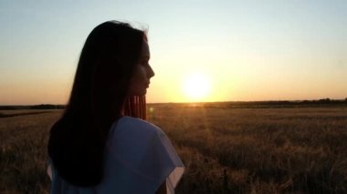 uzun koyu saçlı güzel bir genç kız bir buğday tarlasında duruyor ve uzak bakar. Yaz gün batımına karşı. Kamera arkada uçuyor.